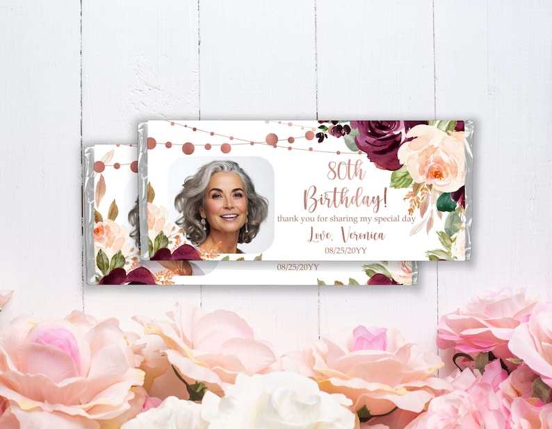 May include: A white chocolate bar wrapper with a floral design in shades of pink, burgundy, and green. The wrapper features a photo of a woman and the text "80th Birthday! thank you for sharing my special day Love. Veronica 08/25/20YY 08/25/20YY".