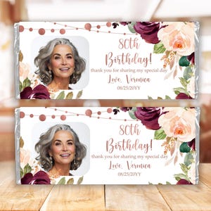 May include: Two chocolate bar wrappers with a floral design in shades of pink, white, and burgundy. The wrappers feature a photo of a woman and the text "80th Birthday! Thank you for sharing my special day. Love, Veronica 08/25/20YY".