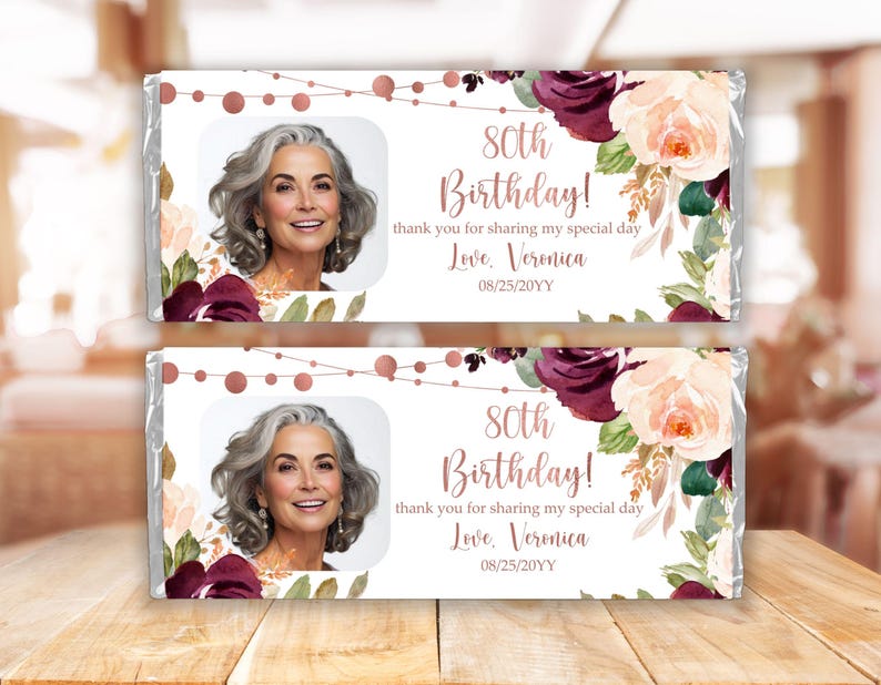 May include: Two chocolate bar wrappers with a floral design in shades of pink, white, and burgundy. The wrappers feature a photo of a woman and the text "80th Birthday! Thank you for sharing my special day. Love, Veronica 08/25/20YY".