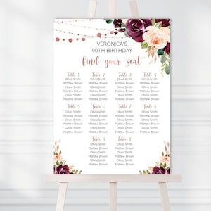 Op de afbeelding: Een wit zitplan met een bloemenontwerp in roze en bordeaux tinten. Het plan vermeldt tafels 1 tot en met 10 met namen voor elke tafel. De tekst bovenaan luidt "Veronica's 90th Birthday find your seat".