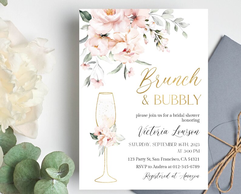 May include: A white invitation with gold lettering for a bridal shower. The invitation features a floral design with pink flowers and green leaves. The text reads "Brunch & Bubbly" and "Victoria Lowson".