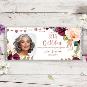 May include: A white chocolate bar wrapper with a floral design in shades of burgundy, pink, and green. The wrapper features a photo of a woman, the text "80th Birthday!" and "thank you for sharing my special day", and the signature "Love, Veronica" with the date "08/25/20YY".
