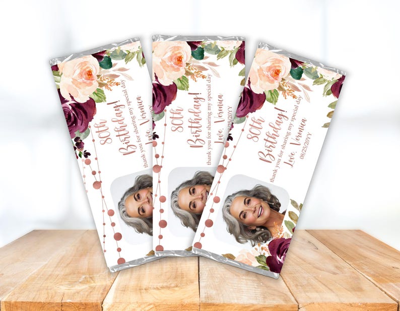 May include: Three chocolate bar wrappers with a floral design in shades of pink and burgundy. The wrappers feature a photo of a woman and the text "80th Birthday!" with a personalized message.