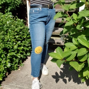 May include: A pair of blue jeans with a yellow crocheted smiley face patch on the knee.