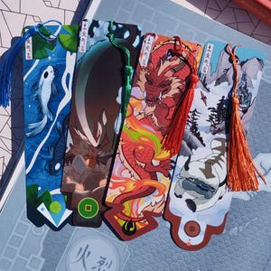 May include: Set of five colorful bookmarks featuring illustrations of fantasy creatures and landscapes. Each bookmark has a tassel in a coordinating color. The designs include a dragon, a flying bison, and other characters.