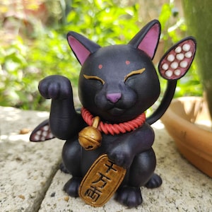 May include: Black Maneki-Neko, a Japanese lucky cat figurine, with a raised paw, red rope necklace with a gold bell, and a gold coin with Japanese characters. The cat has pink ears and a white tail with white spots.