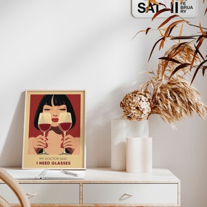 May include: A framed poster with a red background and a woman with black hair holding two glasses of red wine. The text on the poster reads "My doctor said I need glasses."