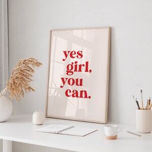 May include: A framed print with a white background and red text that reads "yes girl, you can."