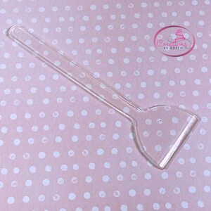 May include: A clear plastic cake scraper with a long handle. The scraper is designed for smoothing out frosting on cakes.