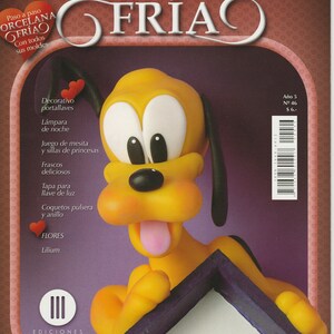May include: A magazine cover featuring a cartoon dog made of yellow porcelain clay. The magazine is titled "Porcelana Fria" and is about crafting with cold porcelain. The dog is holding a small white house with a paw print on the door.