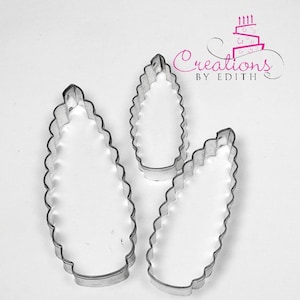 May include: Three metal cookie cutters shaped like pine cones. The cutters are different sizes, with the largest cutter on the left and the smallest cutter on the right.