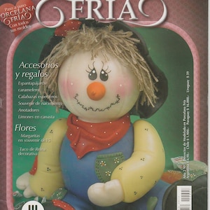 May include: A magazine cover featuring a handmade porcelain doll of a scarecrow with a red bandana and blue overalls. The magazine is titled "Proyectos de modelado en Porcelana Fría" which translates to "Projects of modeling in cold porcelain".