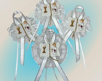 May include: Four white and silver First Communion favours with a white lace design and a small figurine of a child holding a chalice and a book. Each favour has a white satin ribbon with silver trim.