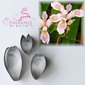 May include: Set of three metal cookie cutters shaped like flower petals. The cutters are silver and have a smooth finish.