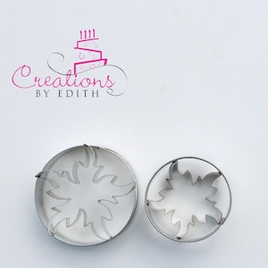 May include: Two metal cookie cutters in the shape of a stylized flower. The larger cutter is on the left and the smaller cutter is on the right.