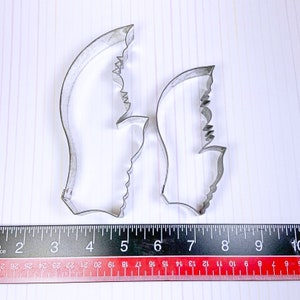 May include: Two metal cookie cutters shaped like butterfly wings. The cutters are made of silver-colored metal and have a serrated edge.