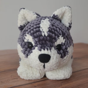 Op de afbeelding: Een pluche speelgoedhond met een grijs en wit vachtpatroon. De hond heeft zwarte ogen en een zwarte neus.