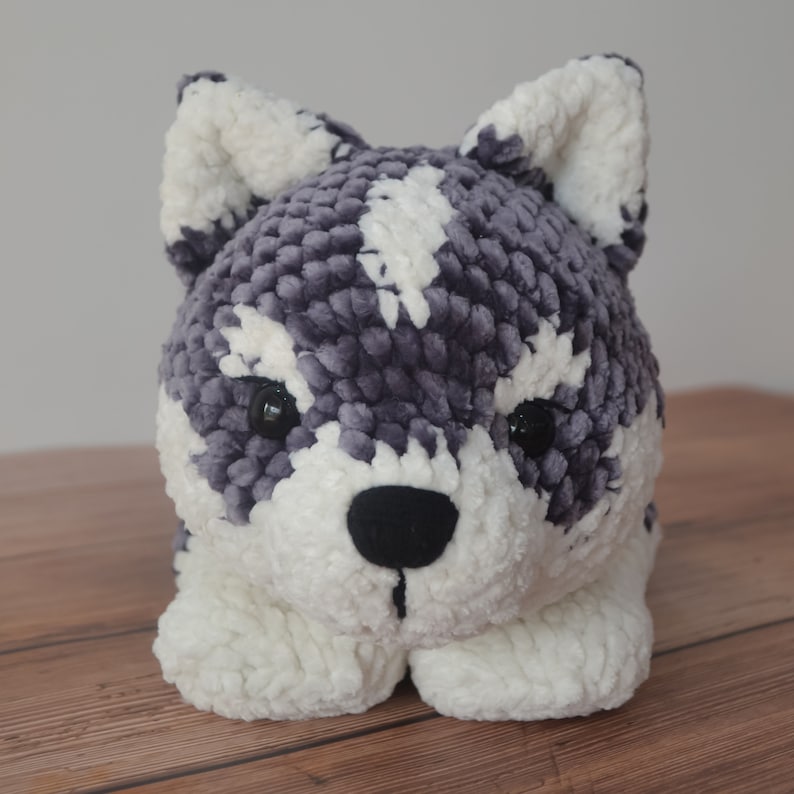 Op de afbeelding: Een pluche speelgoedhond met een grijs en wit vachtpatroon. De hond heeft zwarte ogen en een zwarte neus.