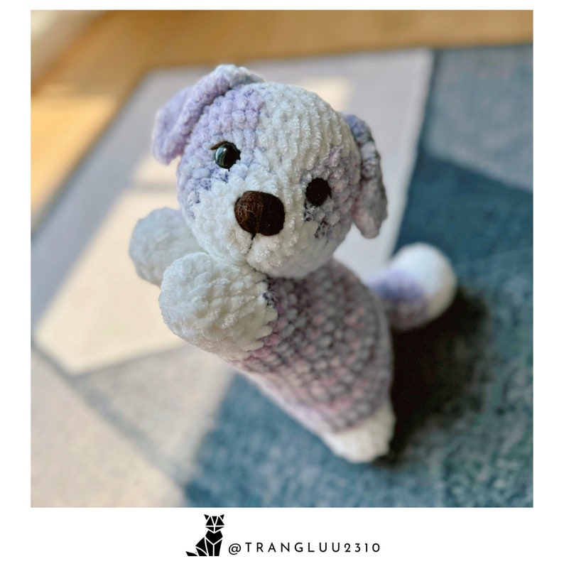 May include: A crocheted plush toy dog with a white and purple color scheme. The dog has a brown nose and black eyes.