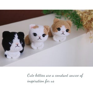 May include: Three handmade crochet cat figurines in black and white, white and tan, and tan and white. The kitties have black eyes and pink noses. The text at the bottom of the image reads: "Cute kitties are a constant source of inspiration for us."