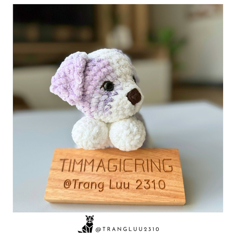 May include: A crocheted purple and white dog toy sitting on a wooden sign with the text "TIMMAGICRING @Trang Luu 2310".