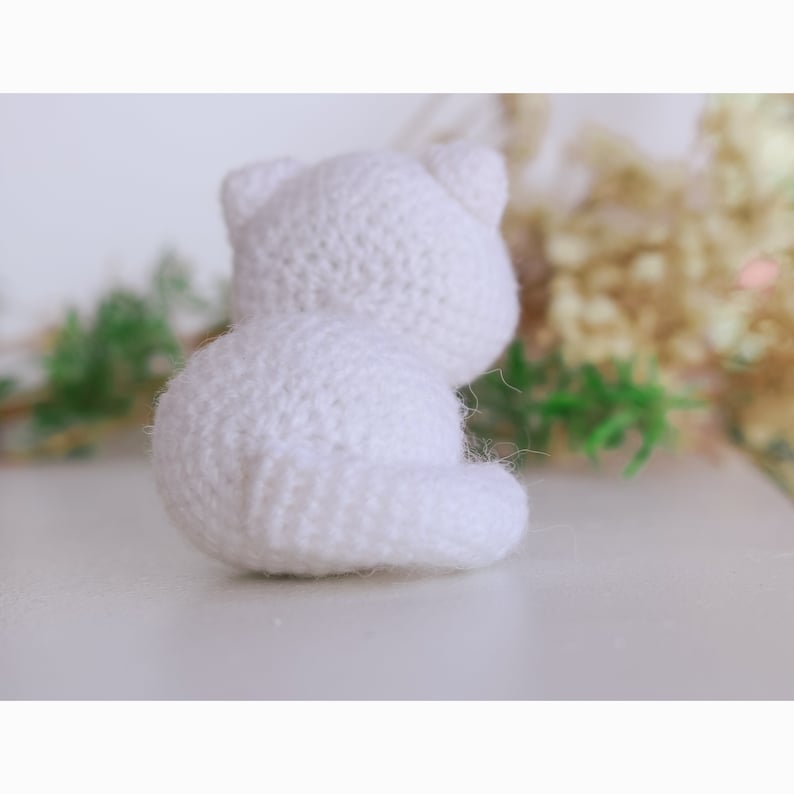 May include: A white crocheted stuffed animal shaped like a cat sitting on a white surface.