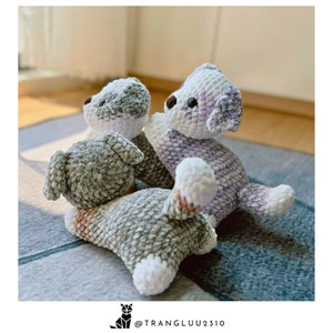 May include: Three crocheted plush dog toys in gray, white, and purple. The dogs are sitting on a gray and blue patterned rug.