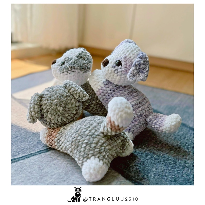 May include: Three crocheted plush dog toys in gray, white, and purple. The dogs are sitting on a gray and blue patterned rug.