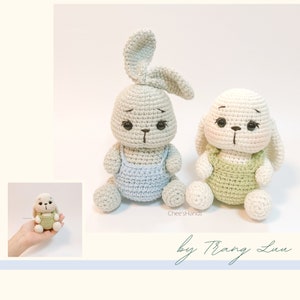 May include: Two crocheted bunny plushies, one gray with blue overalls and one white with green overalls. Both bunnies have black eyes and a brown nose.