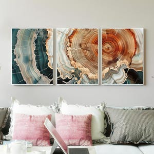 May include: A set of three framed abstract artworks, each depicting a cross-section of wood with natural colours. The art pieces feature shades of teal, brown, and gold. The artworks are mounted on a neutral-toned wall, creating a natural aesthetic.
