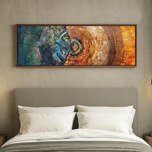 May include: Abstract art piece in a rectangular brown frame. The artwork features a circular design with sections of blue, green, orange, and brown hues. The piece is displayed above a bed with white pillows and a gray headboard.