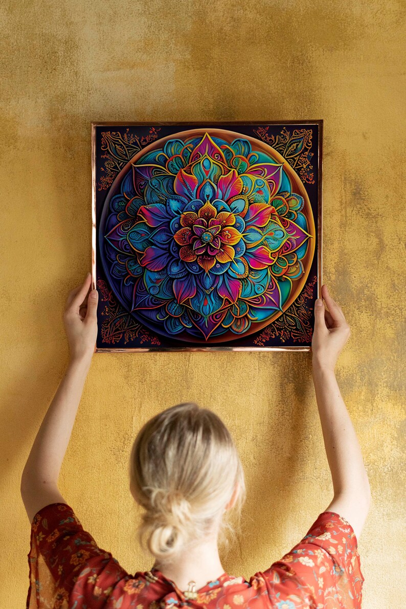 K&ouml;nnte beinhalten: Eine Person h&auml;ngt einen gerahmten Mandala-Druck an einer goldenen Wand. Das Mandala ist ein farbenfrohes kreisf&ouml;rmiges Design mit komplizierten Details. Der Rahmen ist kupferfarben.