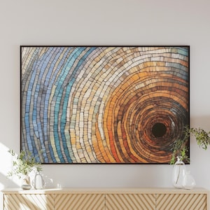 May include: Abstract wall art print featuring a circular pattern of concentric rings in shades of blue, yellow, orange, and brown. The centre of the circle is a dark black hole.