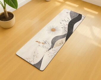 May include: A rectangular yoga mat with a cream-colored background and a floral design. The design includes a sunburst, gray and black wavy shapes, and botanical elements in shades of brown and beige. The mat is on a wooden floor.