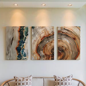 Op de afbeelding: Drie rechthoekige houten kunstpanelen met natuurlijke houtnerfpatronen. De panelen zijn gemonteerd op een witte muur boven een bank. De houtnerf heeft tinten grijs, bruin, oranje en blauw, wat een natuurlijke en artistieke uitstraling creëert.