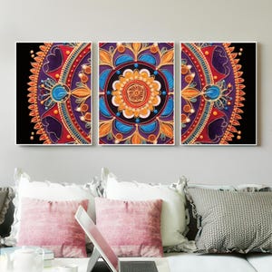 Op de afbeelding: Een drieluik van ingelijste mandala-kunst. Elk paneel heeft een levendig, symmetrisch ontwerp met een zwarte achtergrond. Het kunstwerk toont een cirkelvormig patroon met oranje, blauwe, rode en paarse tinten, waardoor een visueel opvallend en decoratief stuk ontstaat.