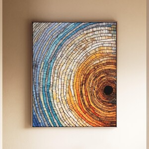 May include: A rectangular wall art piece featuring a mosaic-style pattern of concentric rings. The design transitions from deep blue and light blue on the left to white, yellow, and orange on the right, ending in a solid black circular center.
