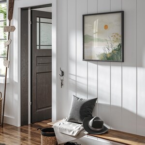 May include: A wooden bench with a gray pillow, a white blanket, a black hat, and a woven basket. The bench is in a hallway with a white wainscoting wall, a dark wood door, and a framed print of a landscape with a sun.