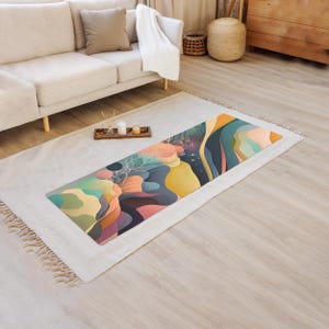 Puede incluir: Una esterilla de yoga colorida con un diseño abstracto que presenta remolinos de azul, verde, amarillo, rosa y naranja. La esterilla está colocada sobre una alfombra blanca con flecos.