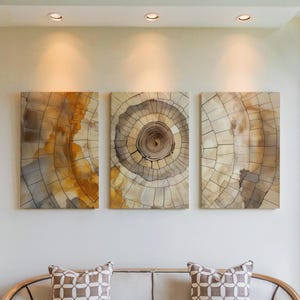May include: Three rectangular wall art pieces depicting cross-sections of trees, showcasing concentric rings in shades of brown, gray, and gold. The artwork hangs above a neutral-toned sofa with patterned throw pillows, creating a natural, earthy aesthetic.