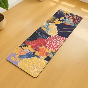 Peut inclure: Un tapis de yoga rectangulaire avec un fond bleu foncé et un motif floral. Les fleurs sont dans des tons de jaune, de rouge et d'orange. Le tapis est sur un sol en bois clair.