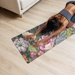 May include: A floral yoga mat featuring a dark background with large, colorful flowers in shades of pink, orange, and yellow. The mat is rectangular and appears to be in use on a light wood floor.