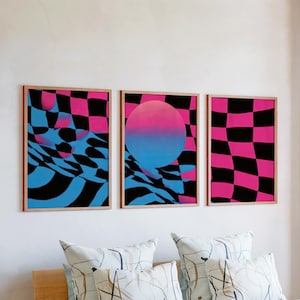 May include: Three framed abstract art prints. The artwork features a checkerboard pattern in black and pink, with a blue and pink gradient sphere in the center print. The frames are a light brown color.
