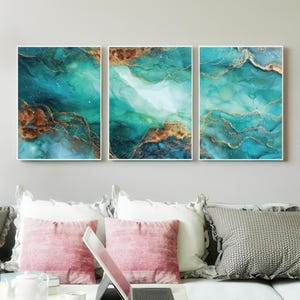 May include: Three framed abstract art pieces with teal, gold, and brown tones. The artwork features fluid designs with gold veins, creating a marbled effect. The pieces are displayed above a couch with pink and gray pillows.