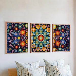 May include: Three framed artworks featuring colourful circular patterns in shades of blue, orange, yellow, and green. The art is displayed above decorative cushions, creating a vibrant interior design.
