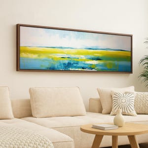 May include: Abstract landscape painting in a dark brown frame. The artwork features a vibrant mix of yellow, blue, and white hues, evoking a sense of nature. The painting hangs above a beige sectional sofa with decorative pillows.