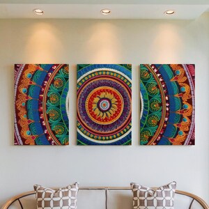 May include: Three rectangular wall art pieces with colorful mandala designs. The artwork features intricate patterns in shades of blue, orange, green, and purple. The central piece has a circular design with a yellow center. The art is displayed on a white wall.