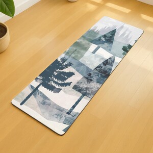 Peut inclure: Tapis de yoga rectangulaire avec un motif inspiré de la nature. Le tapis présente un motif d'arbres stylisés, de montagnes et de formes géométriques dans des tons de bleu, de vert et de blanc. Le tapis est posé sur un sol en bois.