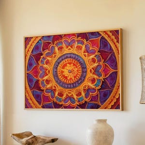 May include: A framed, colorful mandala art print. The artwork features a symmetrical design with shades of red, orange, purple, and gold. The mandala is centered on a light-colored wall, with a neutral-toned curtain and decorative elements in the foreground.