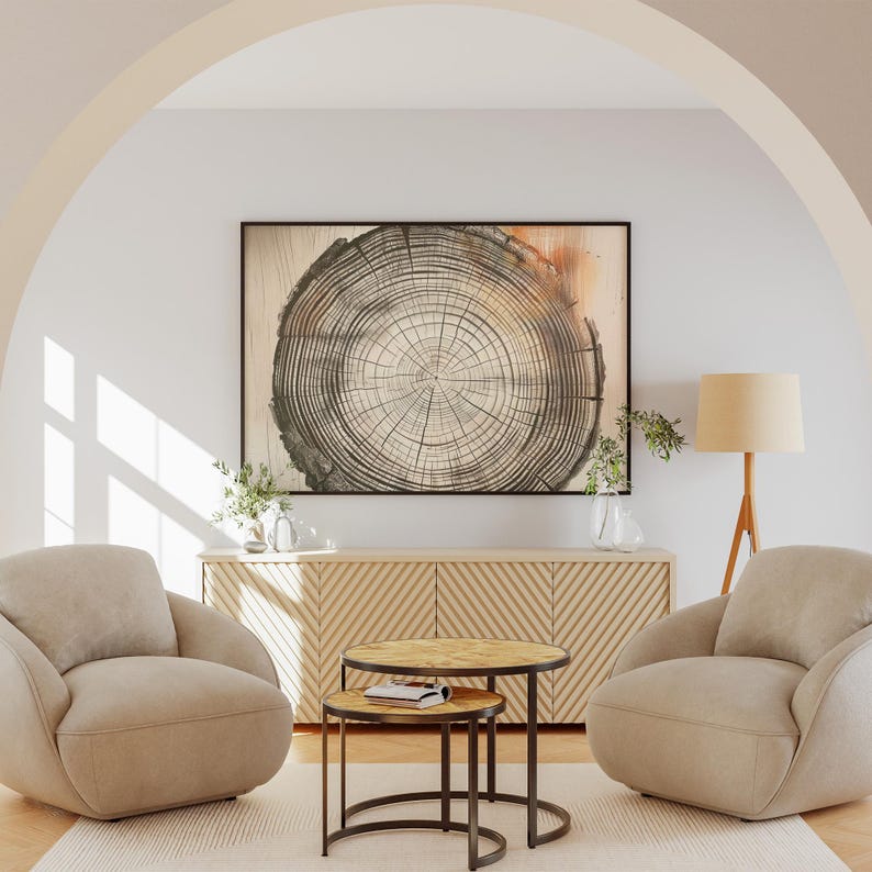 Pode incluir: Duas poltronas bege com uma mesa de centro de madeira em uma sala de estar com uma grande impress&atilde;o emoldurada de uma se&ccedil;&atilde;o transversal de tronco de &aacute;rvore sobre um arm&aacute;rio de madeira.